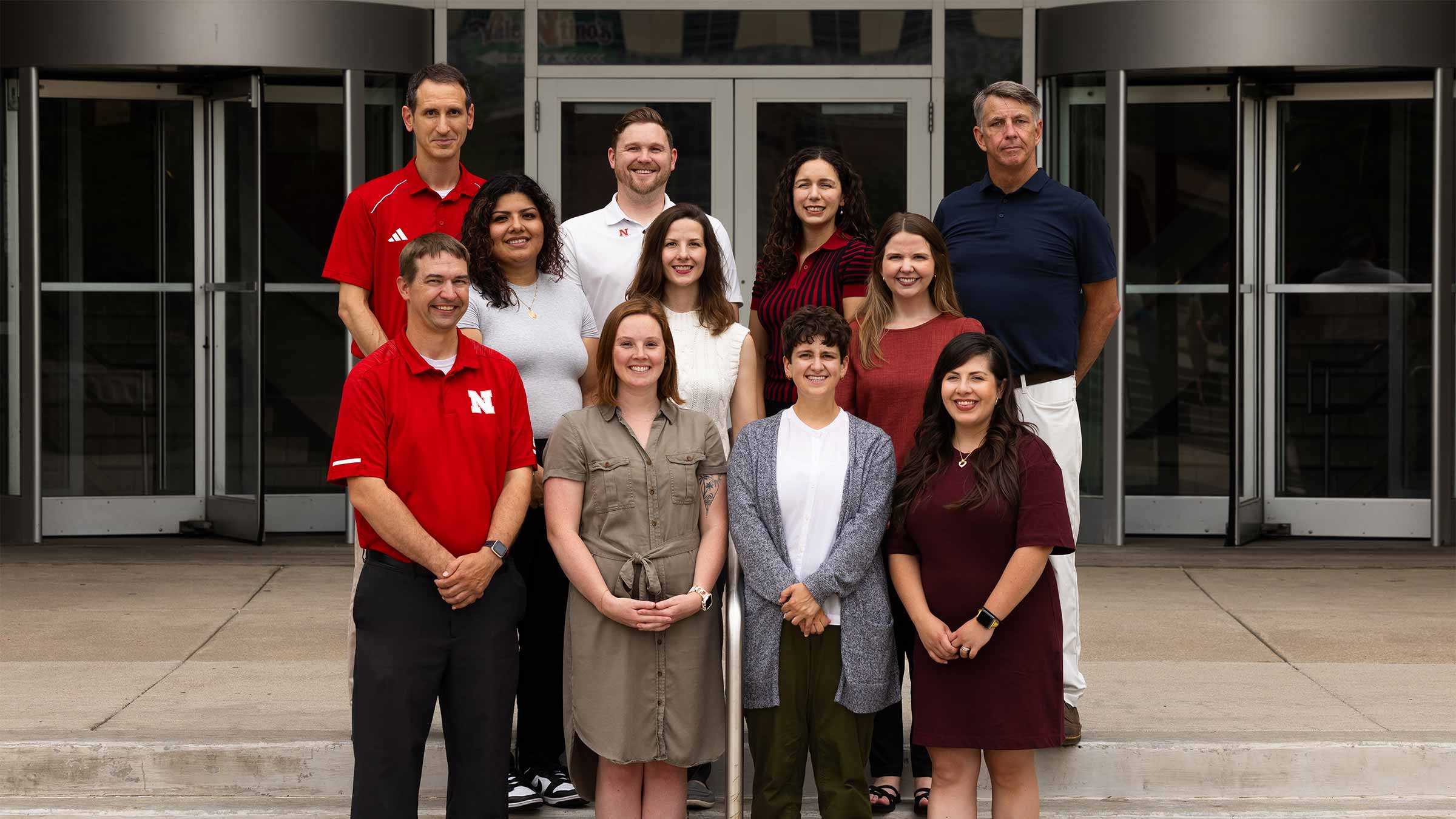 Academic Navigator staff standing outside a building with glass doors, dressed in various professional attire.