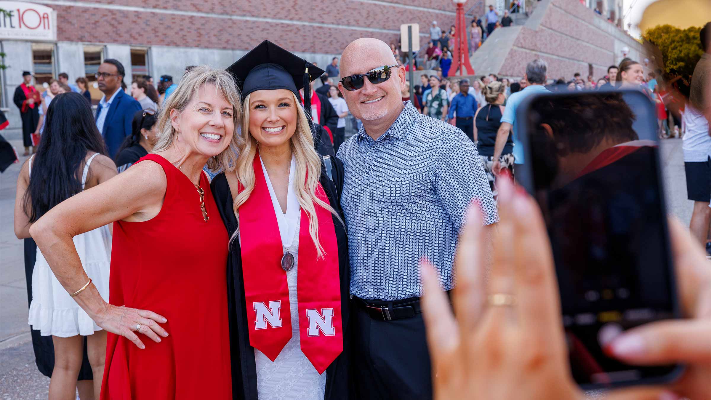 Graduation celebration with smiling graduate in cap and gown with parents.