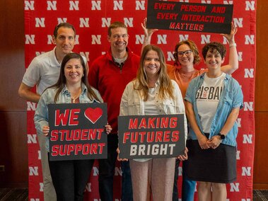 Academic Navigator team holding supportive signs against a backdrop with repeated red "N" logos.